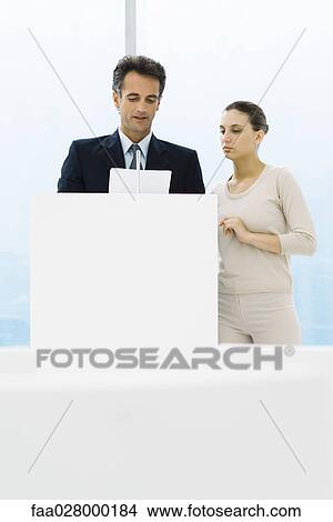Businessman standing at lectern, discussing document with female assistant View Large Photo Image Picture - Businessman standing at lectern, discussing document with female assistant. Fotosearch