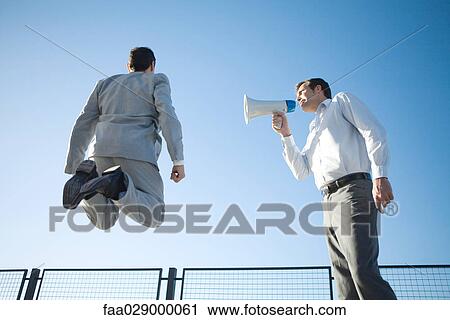Businessman standing beside colleague, shouting into megaphone, colleague jumping in air, low angle view View Large Photo Image Stock Image - Businessman standing beside colleague, shouting into megaphone, colleague jumping in air, low angle view. Fotosearch