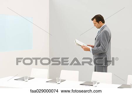Picture - Businessman standing beside conference table, reading newspaper. Fotosearch