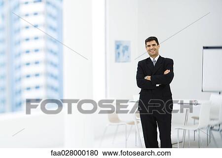 Businessman standing in office with arms folded, smiling at camera View Large Photo Image Stock Image - Businessman standing in office with arms folded, smiling at camera. Fotosearch