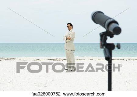 Businessman standing on beach with arms folded, telescope pointed at him in foreground View Large Photo Image Stock Image - Businessman standing on beach with arms folded, telescope pointed at him in foreground. Fotosearch