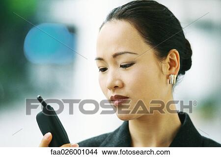 Businesswoman looking down at cell phone, close-up View Large Photo Image Picture - Businesswoman looking down at cell phone, close-up. Fotosearch