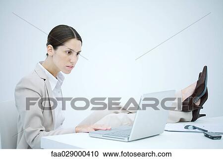 Businesswoman sitting at desk with legs up, using laptop View Large Photo Image Stock Image - Businesswoman sitting at desk with legs up, using laptop. Fotosearch