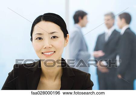 Businesswoman smiling at camera, male colleagues standing in background View Large Photo Image Stock Photograph - Businesswoman smiling at camera, male colleagues standing in background. Fotosearch