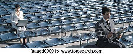 Stock Photography - Businesswoman using laptop, businessman reading newspaper on bleachers. Fotosearch