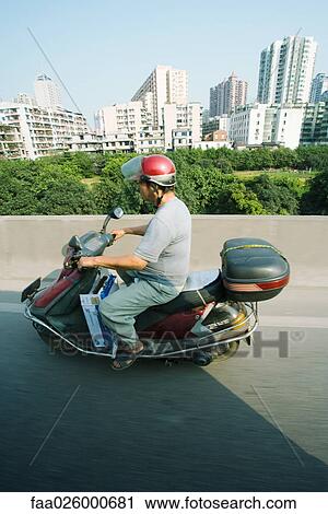 China, Guangzhou, man riding motor scooter, high-rise buildings in background, side view View Large Photo Image Stock Image - China, Guangzhou, man riding motor scooter, high-rise buildings in background, side view. Fotosearch