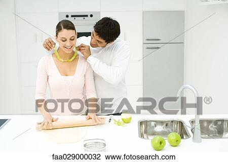 Couple baking in kitchen, man holding apple peel around woman's neck View Large Photo Image Stock Image - Couple baking in kitchen, man holding apple peel around woman's neck. Fotosearch