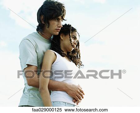 Couple embracing outdoors, looking away, low angle view View Large Photo Image Stock Photography - Couple embracing outdoors, looking away, low angle view. Fotosearch