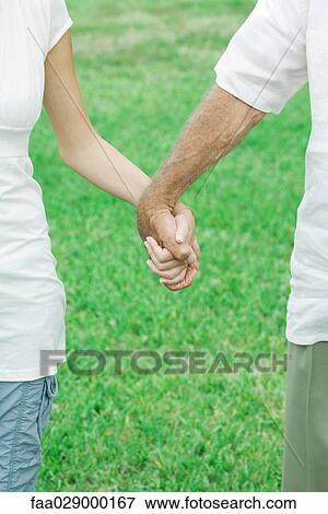 Stock Photo - Couple holding hands outdoors, cropped view. Fotosearch
