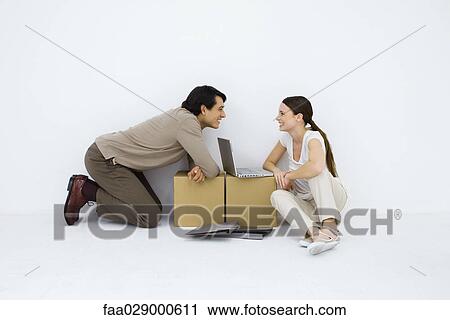 Couple sitting at makeshift desk with laptop computer between them, smiling at each other View Large Photo Image Stock Image - Couple sitting at makeshift desk with laptop computer between them, smiling at each other. Fotosearch