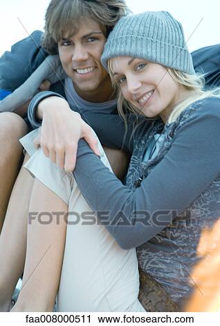 Stock Image - Couple sitting close together, smiling at camera. Fotosearch