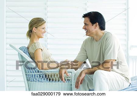 Couple sitting face to face on porch, smiling, woman touching man's arm View Large Photo Image Stock Photo - Couple sitting face to face on porch, smiling, woman touching man's arm. Fotosearch