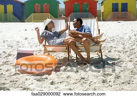 Couple sitting in lounge chairs at the beach, smiling, woman's legs on man's lap View Large Photo Image Stock Image - Couple sitting in lounge chairs at the beach, smiling, woman's legs on man's lap. Fotosearch