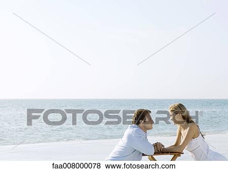 Stock Photo - Couple sitting on beach, gazing at each other. Fotosearch
