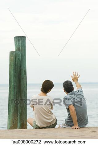 Couple sitting on edge of dock, man waving View Large Photo Image Stock Image - Couple sitting on edge of dock, man waving. Fotosearch