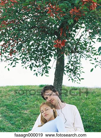 Couple sitting under tree listening to earphones, portrait View Large Photo Image Stock Photo - Couple sitting under tree listening to earphones, portrait. Fotosearch