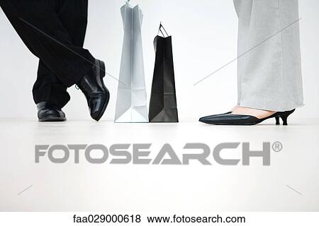 Stock Photo - Couple standing with shopping bags between them, cropped view of feet, low angle view. Fotosearch