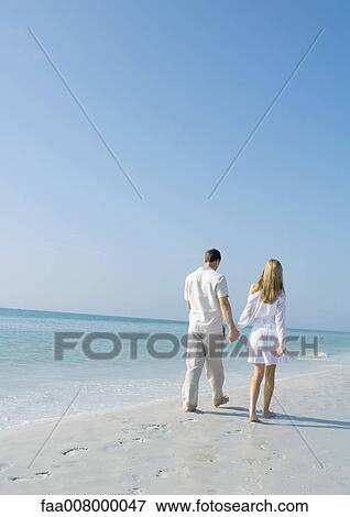 Couple walking on beach, rear view View Large Photo Image Stock Photo - Couple walking on beach, rear view. Fotosearch