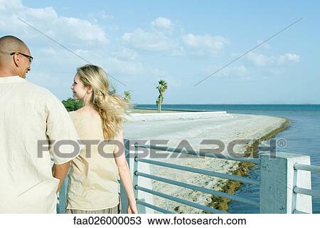 Couple walking together at the beach, looking at each other, rear view View Large Photo Image Stock Image - Couple walking together at the beach, looking at each other, rear view. Fotosearch
