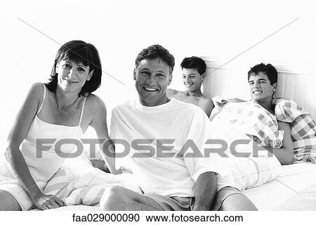 Family sitting on bed together, man and woman smiling at camera View Large Photo Image Stock Image - Family sitting on bed together, man and woman smiling at camera. Fotosearch