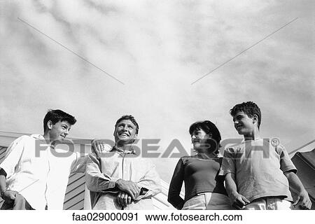 Family standing side by side outdoors, smiling, man looking up View Large Photo Image Stock Image - Family standing side by side outdoors, smiling, man looking up. Fotosearch