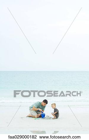 Stock Image - Father and son at the beach, playing with sand bucket. Fotosearch
