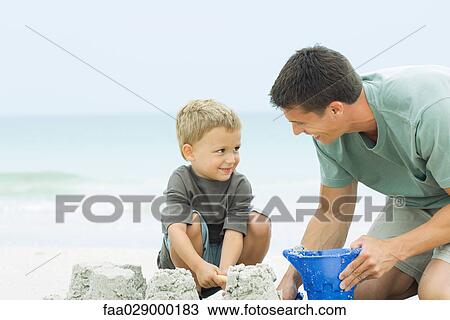 Father and son playing with sand bucket at the beach, smiling at each other View Large Photo Image Stock Image - Father and son playing with sand bucket at the beach, smiling at each other. Fotosearch