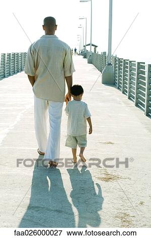 Father and son walking together, holding hands, rear view View Large Photo Image Stock Photo - Father and son walking together, holding hands, rear view. Fotosearch
