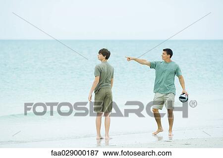Father and teen son at the beach, man holding ball and pointing, both looking away View Large Photo Image Stock Photo - Father and teen son at the beach, man holding ball and pointing, both looking away. Fotosearch