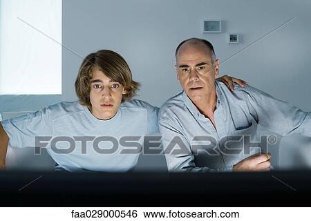 Father and teen son watching TV together, boy's arm around man's shoulder View Large Photo Image Stock Photograph - Father and teen son watching TV together, boy's arm around man's shoulder. Fotosearch