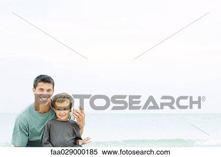 Father holding seashell up to son's ear at the beach, smiling at camera View Large Photo Image Stock Photography - Father holding seashell up to son's ear at the beach, smiling at camera. Fotosearch