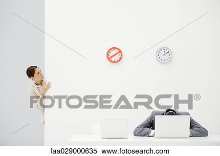 Female office worker peeking around corner at clocks on wall, colleague sitting in front of laptop with head down View Large Photo Image Stock Photography - Female office worker peeking around corner at clocks on wall, colleague sitting in front of laptop with head down. Fotosearch