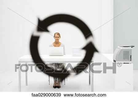 Female professional sitting in office, looking at camera through arrow symbol in foreground View Large Photo Image Stock Photo - Female professional sitting in office, looking at camera through arrow symbol in foreground. Fotosearch