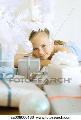 Stock Photograph - Girl lying under christmas tree among presents. Fotosearch