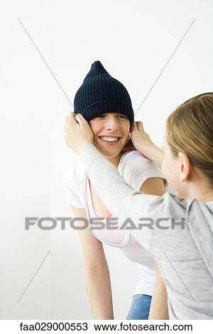Stock Image - Girl pulling knit hat over her friend's head. Fotosearch