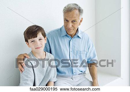 Grandfather sitting with arm around grandson's shoulder, both smiling at camera, portrait View Large Photo Image Stock Photography - Grandfather sitting with arm around grandson's shoulder, both smiling at camera, portrait. Fotosearch
