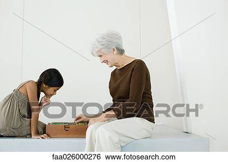 Grandmother and granddaughter sitting face to face, playing board game together, side view View Large Photo Image Stock Photograph - Grandmother and granddaughter sitting face to face, playing board game together, side view. Fotosearch