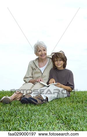 Grandmother and grandson sitting in grass with book, both looking away and smiling View Large Photo Image Stock Photo - Grandmother and grandson sitting in grass with book, both looking away and smiling. Fotosearch