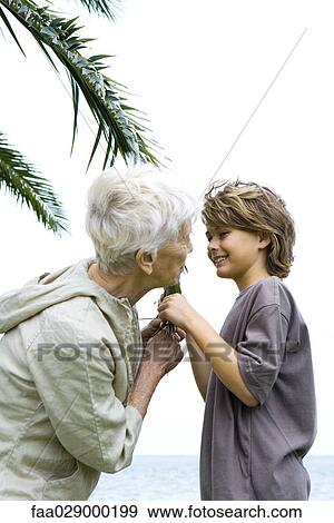 Grandmother and grandson standing face to face, holding palm leaf, smiling at each other View Large Photo Image Stock Photo - Grandmother and grandson standing face to face, holding palm leaf, smiling at each other. Fotosearch