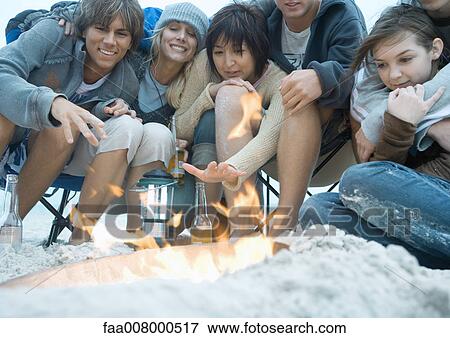 Group of young adult friends, sitting around campfire on beach, reaching hands toward fire View Large Photo Image Stock Photo - Group of young adult friends, sitting around campfire on beach, reaching hands toward fire. Fotosearch