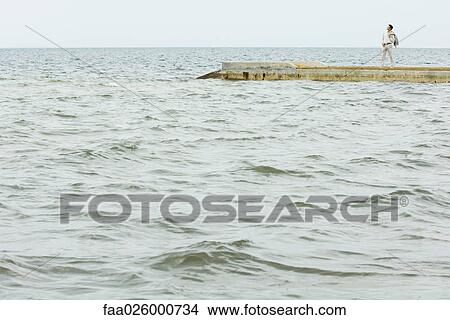 In the distance, man standing on jetty, surrounded by sea View Large Photo Image Picture - In the distance, man standing on jetty, surrounded by sea. Fotosearch