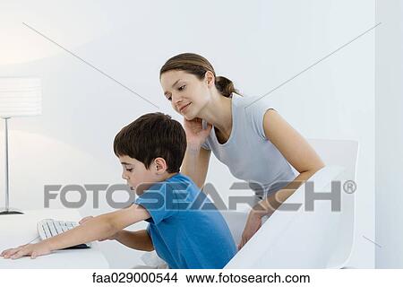 Picture - Little boy using computer keyboard, mother watching over his shoulder. Fotosearch