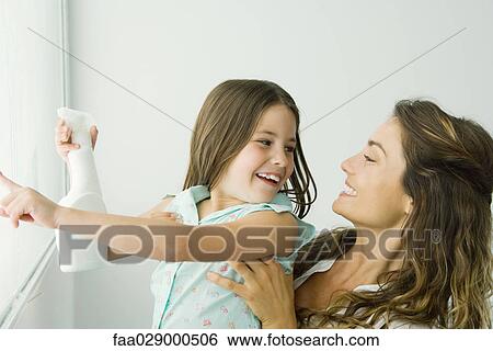 Stock Photograph - Little girl cleaning window, pointing, smiling at mother. Fotosearch