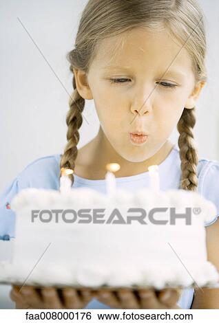 Stock Photograph - Little girl holding birthday cake, blowing out candles. Fotosearch