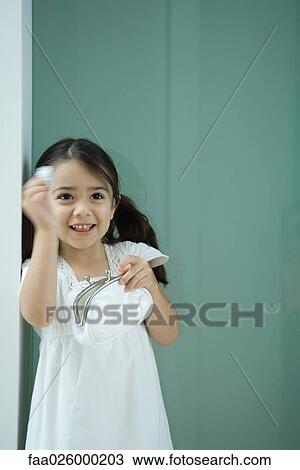 Stock Image - Little girl holding coin purse, one hand raised, smiling. Fotosearch