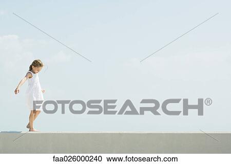 Little girl walking across low wall, arms out, looking down View Large Photo Image Stock Image - Little girl walking across low wall, arms out, looking down. Fotosearch