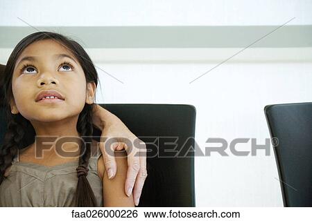 Stock Photograph - Little girl with woman's hand on her shoulder, looking up, close-up. Fotosearch
