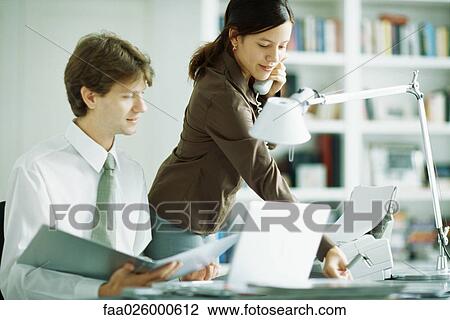 Male and female colleagues at desk, man looking at laptop computer, woman using phone View Large Photo Image Stock Image - Male and female colleagues at desk, man looking at laptop computer, woman using phone. Fotosearch