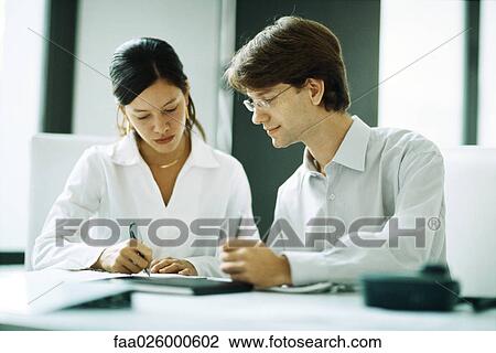 Male and female colleagues sitting together at desk, both writing, looking down View Large Photo Image Stock Image - Male and female colleagues sitting together at desk, both writing, looking down. Fotosearch