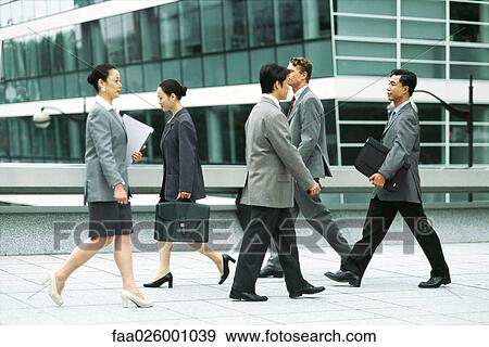 Stock Photo - Male and female professionals walking on busy sidewalk, side view. Fotosearch